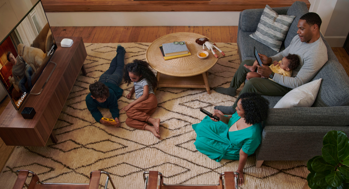 Family using various devices in a cozy living room, with children playing on the floor and adults relaxing on the couch and carpet